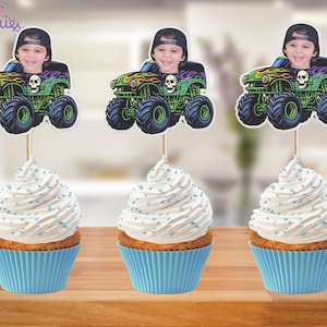 May include: Three cupcakes with blue liners and white frosting, each topped with a monster truck image featuring a child's face. The monster trucks are green, black, and orange with skull details. The cupcakes sit on a wooden surface.