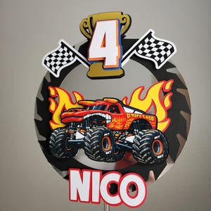 Pode incluir: Topper de bolo de caminh&atilde;o monstro vermelho e laranja com o texto "El Toro Loco" e "NICO". Inclui um trof&eacute;u dourado, o n&uacute;mero 4 e bandeiras quadriculadas. O fundo &eacute; uma l&acirc;mina de serra preta e prateada.