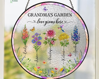 May include: A circular hanging suncatcher with a textured glass surface featuring the text "GRANDMA'S GARDEN love grows here". It displays five colorful floral stems labeled with the names Emily, Anna, Penelope, Kelvin, and Jack, accented by butterflies and a hummingbird.