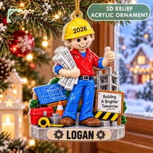 May include: A 3D relief acrylic ornament featuring a construction worker in a yellow hard hat labeled 2026, holding blueprints. The base displays the name LOGAN and a sign reading Building A Brighter Tomorrow, with a red toolbox and tape measure.
