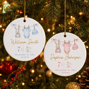 May include: Two round white ceramic ornaments featuring watercolor illustrations of a bunny, a onesie, and a hat hanging on a clothesline. One ornament displays the name William Smith with birth details 7 lbs 6 oz, 21 in, December 30, 2026, 05:50AM. The other shows Sophia Johnson with identical birth data.