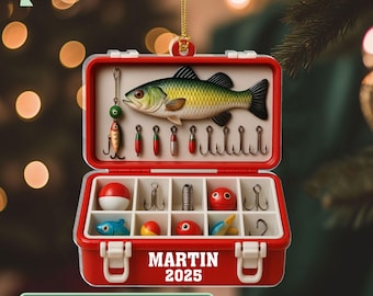 May include: A red and white fishing tackle box Christmas ornament. The ornament features a detailed illustration of a fish, fishing lures, and hooks. The text "MARTIN 2025" is displayed on the front, with the text "2D FLAT ACRYLIC NOT 3D" below.
