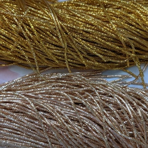 May include: Two spools of metallic thread, one gold and one silver. The thread is thin and shiny, and it is wound tightly around the spools.