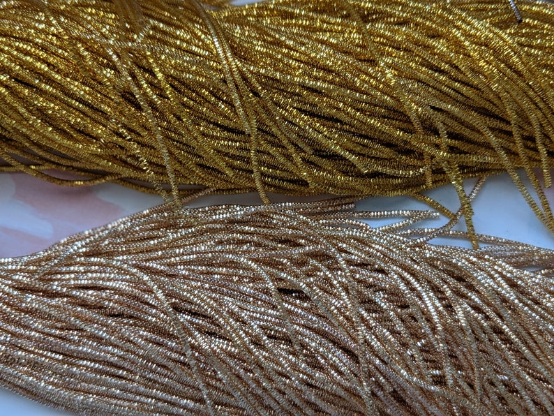 May include: Two spools of metallic thread, one gold and one silver. The thread is thin and shiny, and it is wound tightly around the spools.