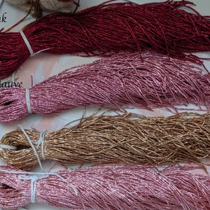 May include: Four spools of metallic seed beads in different colors: hot pink, pink mauve, hazel, and rose. The beads are arranged in a row, with the hot pink beads at the top and the rose beads at the bottom.
