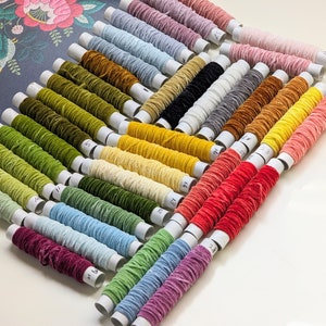 May include: A collection of 30 spools of embroidery floss in various colors, including green, yellow, red, blue, and pink. Each spool is labeled with a number.