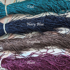 May include: Four spools of metallic seed beads in teal, navy blue, graphite, and plum colors. The beads are arranged in rows, with the teal beads at the top and the plum beads at the bottom.