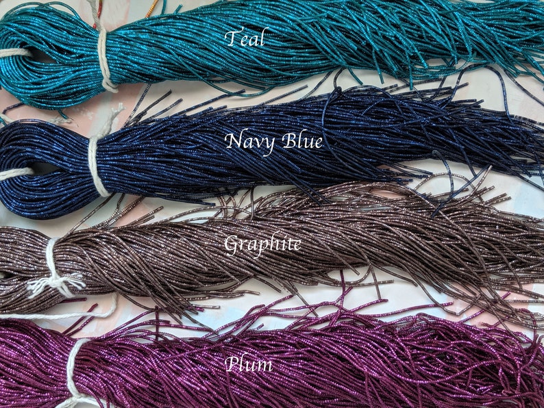 May include: Four spools of metallic seed beads in teal, navy blue, graphite, and plum colors. The beads are arranged in rows, with the teal beads at the top and the plum beads at the bottom.