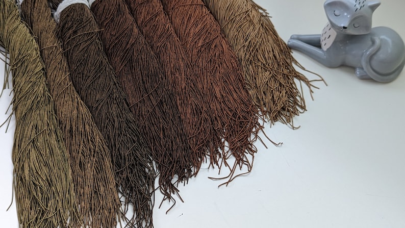 Peut inclure: Une collection de huit bobines de cordon &eacute;lastique brun et vert, dispos&eacute;es en d&eacute;grad&eacute; du vert fonc&eacute; au brun clair.