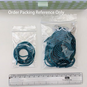May include: Two clear plastic bags containing teal colored string. The smaller bag contains a single coil of string, while the larger bag contains a larger quantity of string.
