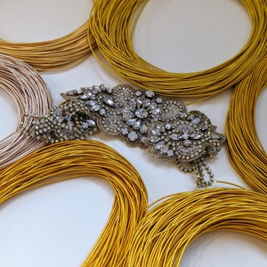 May include: A close-up of a sparkly, silver, rhinestone brooch with a floral design. The brooch is surrounded by several spools of gold thread.