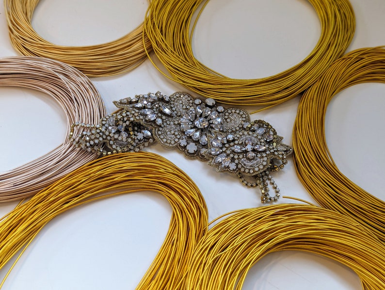 May include: A close-up of a sparkly, silver, rhinestone brooch with a floral design. The brooch is surrounded by several spools of gold thread.