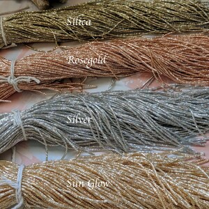 May include: Four spools of metallic thread in different colors: gold, rose gold, silver, and a light gold color labeled "Sun Glow". The spools are labeled with the color names.