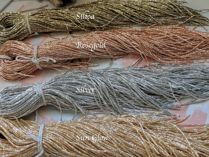 May include: Four spools of metallic thread in different colors: gold, rose gold, silver, and a light gold color labeled "Sun Glow". The spools are labeled with the color names.