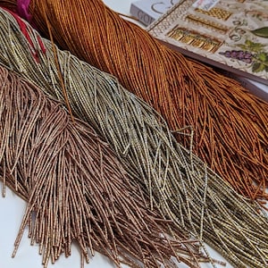 May include: Three strands of metallic beads in shades of copper, gold, and silver. The beads are long and thin, resembling strands of hair.