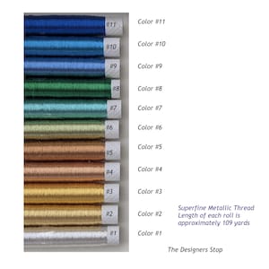 Op de afbeelding: Een collectie van elf spoelen superfijn metallic garen verticaal gerangschikt, gelabeld Color #1 tot Color #11. De garens vari&euml;ren in kleur van wit, goud, koper, brons, groen en diverse tinten blauw. Elke rol is ongeveer 100 meter lang.
