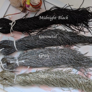 May include: Four spools of metallic seed beads in different colors: Midnight Black, Gunmetal, Gray, and Steel. The beads are arranged in a row, with the darkest color at the top and the lightest color at the bottom.