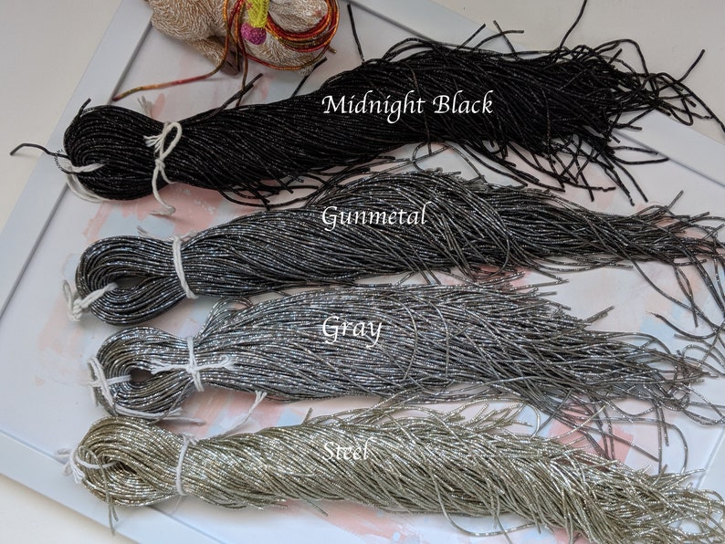 May include: Four spools of metallic seed beads in different colors: Midnight Black, Gunmetal, Gray, and Steel. The beads are arranged in a row, with the darkest color at the top and the lightest color at the bottom.