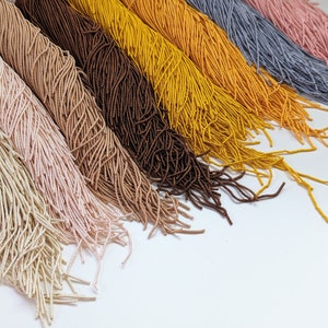 May include: A collection of ten strands of colorful embroidery floss, each in a different color. The colors include beige, light pink, brown, yellow, gold, orange, gray, light blue, pink, and red.
