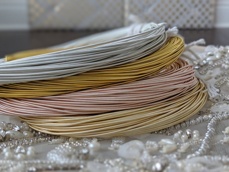 May include: Four spools of metallic wire in silver, gold, rose gold, and a lighter gold color. The spools are stacked on top of each other.