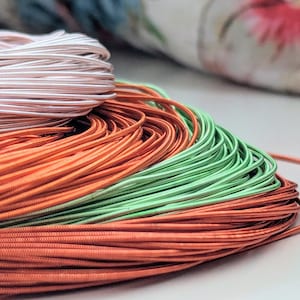 May include: A close-up of three spools of cord. The top spool is silver, the middle spool is orange, and the bottom spool is green.