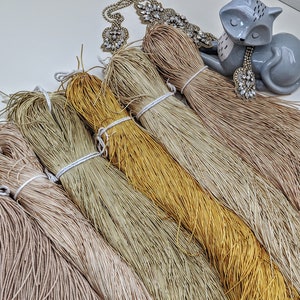 May include: A collection of six spools of natural fiber cord in various shades of beige, brown, and gold. The cords are arranged in a fan shape, with the ends of the cords extending out from the center.