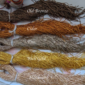 May include: Five spools of metallic seed beads in various colors, including Old Bronze, Cider, Tan, Rich Gold, and Macaroon. The beads are arranged in a row on a white surface.