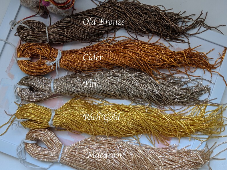 May include: Five spools of metallic seed beads in various colors, including Old Bronze, Cider, Tan, Rich Gold, and Macaroon. The beads are arranged in a row on a white surface.