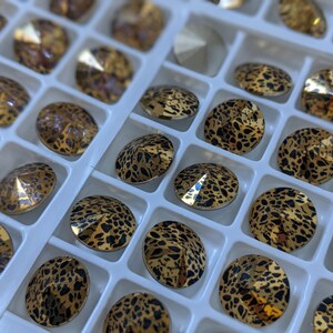 May include: A close-up of a tray filled with small, round, gold-toned rhinestones. The rhinestones have a black leopard print design.