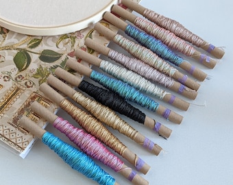 May include: A collection of colorful embroidery floss spools wrapped in brown paper with purple tape. The floss is wound around cardboard spools and is ready for use in embroidery projects.