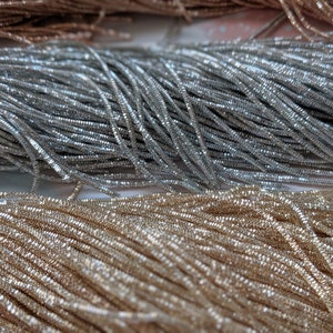 May include: Close-up of silver and gold metallic thread spools. The thread is shiny and has a textured surface.