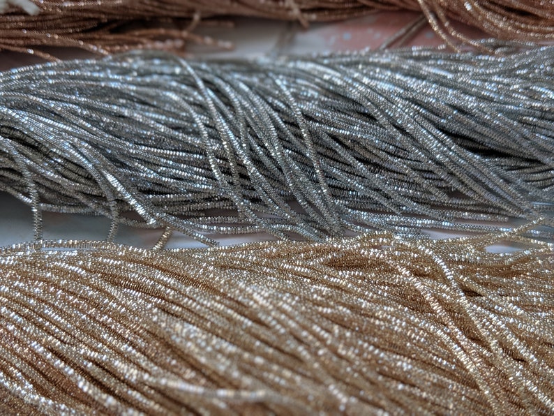 May include: Close-up of silver and gold metallic thread spools. The thread is shiny and has a textured surface.