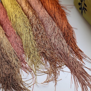 May include: A collection of eight strands of metallic yarn in shades of brown, gold, and orange. The yarn is arranged in a fan shape, with the ends of the strands fanned out.