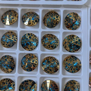 May include: A close-up of a tray of round, iridescent blue and gold rhinestones. The rhinestones are arranged in a grid pattern and have a textured, speckled surface.
