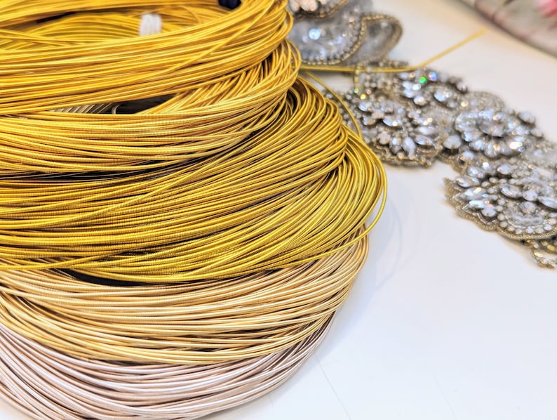 May include: Close-up of a spool of gold and silver metallic thread. The thread is wound tightly around the spool, creating a spiral pattern.