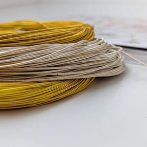 Könnte beinhalten: Spulen aus Metalldraht in Gold- und Silbertönen. Der Draht weist eine texturierte, gewickelte Oberfläche auf und ist in gestapelten kreisförmigen Schleifen angeordnet. Der goldene Draht liegt oben und unten, der silberne Draht in der Mitte.
