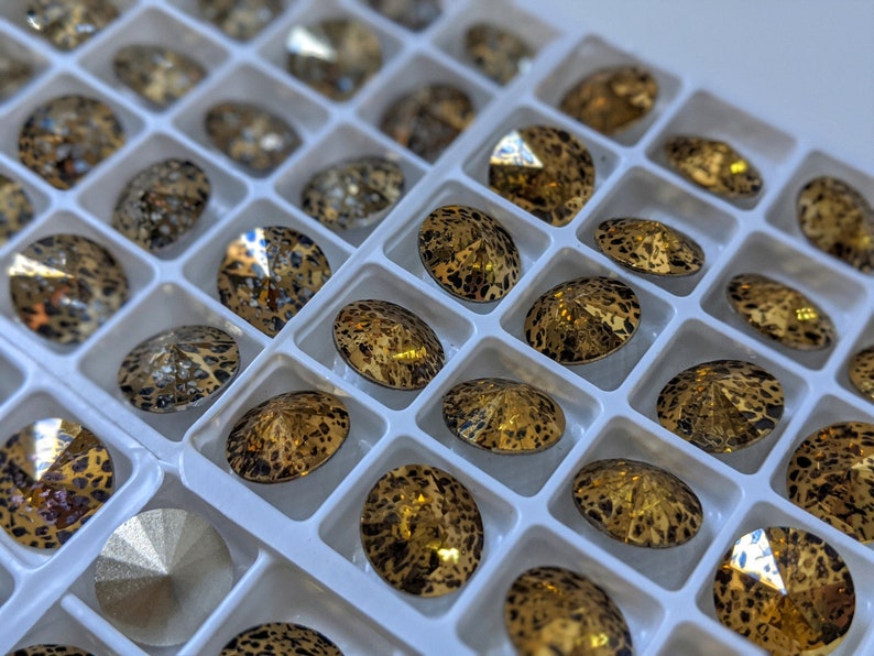 May include: A close-up of a tray of gold and black rhinestones. The rhinestones are arranged in a grid pattern and have a leopard print design.