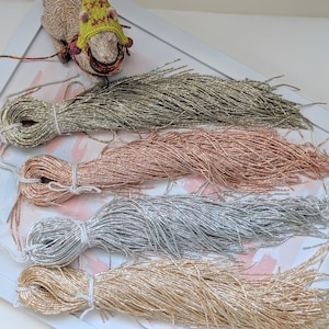 May include: Four spools of metallic thread in gold, silver, rose gold, and green. The thread is arranged in a fan shape on a white surface.