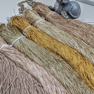 May include: A collection of six spools of metallic thread in various shades of beige, gold, and brown. The thread is arranged in a fan shape, with the ends of the thread extending out from the spools.