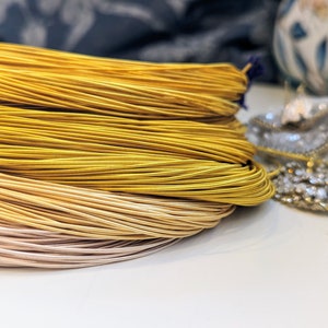May include: A close-up of a pile of gold and beige cord, likely used for jewelry making or crafting.