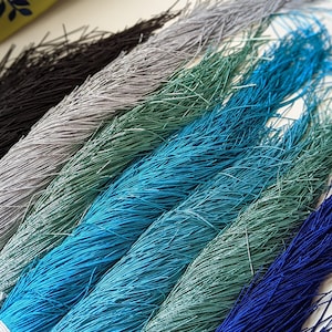 Peut inclure: Assortiment de cordons colorés en noir, argent, bleu sarcelle, bleu, vert et marine. Les cordons sont regroupés et ont une texture effilochée.