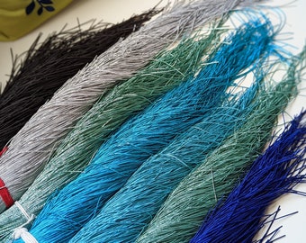 Puede incluir: Surtido de cordones coloridos en negro, plateado, azul verdoso, azul, verde y azul marino. Los cordones están agrupados y tienen una textura deshilachada.