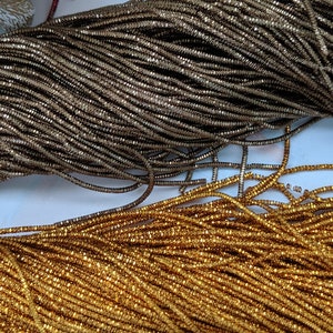 May include: Two spools of metallic thread, one gold and one silver. The thread is made of small, square-shaped beads.
