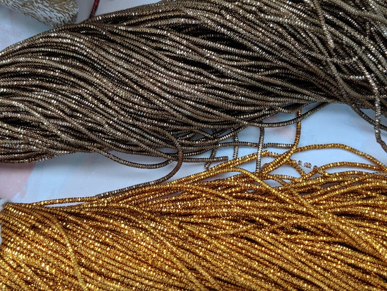 May include: Two spools of metallic thread, one gold and one silver. The thread is made of small, square-shaped beads.