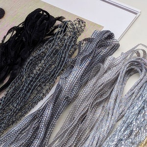 以下が含まれることがあります： 黒、グレー、シルバー、ゴールドの金属製のトリムの詰め合わせ。トリムはレース、リボン、コードなど、さまざまな素材で作られています。