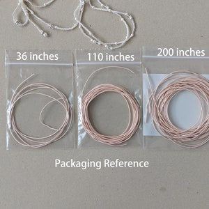 May include: Three clear plastic bags with pink string spools inside. The bags are labeled with the lengths of the string: 36 inches, 110 inches, and 200 inches. The text "Packaging Reference" is printed below the bags.