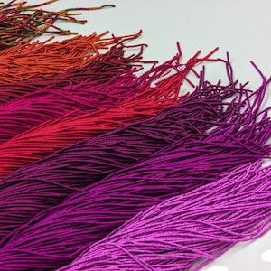 May include: A collection of colorful embroidery floss spools arranged in a gradient from orange to purple. The floss is arranged in a fan shape, with the ends of the floss strands fanned out.