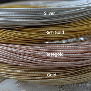 May include: Close-up of four spools of wire in different metallic colors: silver, rich gold, rose gold, and gold. The wire is coiled and stacked on top of each other.