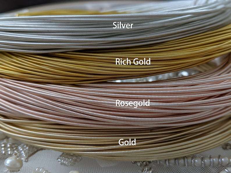 May include: Close-up of four spools of wire in different metallic colors: silver, rich gold, rose gold, and gold. The wire is coiled and stacked on top of each other.