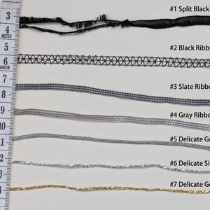 May include: Seven different types of ribbon, including split black, black ribbon, slate ribbon, gray ribbon, delicate gray, delicate silver, and delicate gold. The ribbons are laid out horizontally on a white surface with a ruler in the left side of the image.